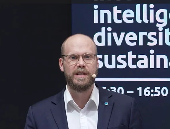 Christian Völl als Redner mit Headset-Mikrofon auf einer Konferenzbühne.
